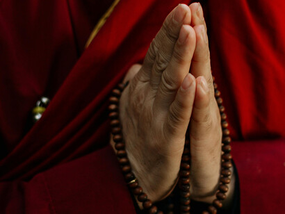 A pair of hands in prayer, holding beads
