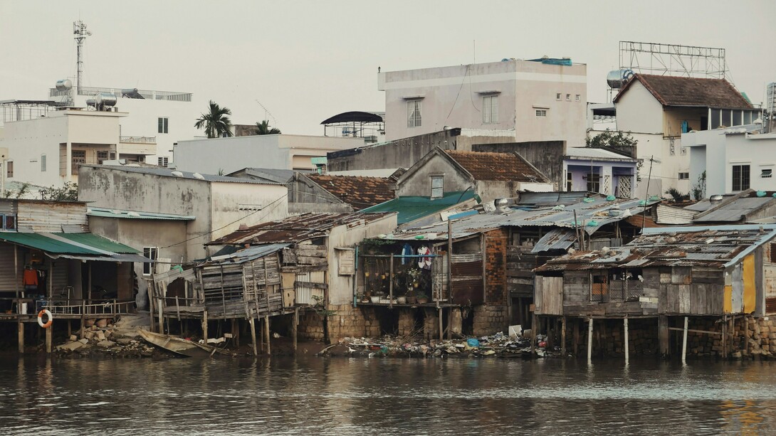 L'image présente des habitations traditionnelles sur pilotis en bordure d'un cours d'eau, typiques des paysages fluviaux du delta du Mékong au Vietnam