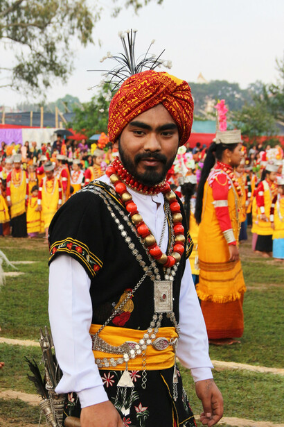 A Khasi man in traditional attire alongside performers in vibrant traditional costumes during a cultural parade in Meghalaya, India