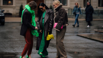 Estilista encontra as amigas enquanto usa um cachecol verde na forma de uma corrente em alusão ao compromisso com a sustentabilidade