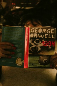 Person sitting and reading George Orwell’s 1984, surrounded by a dim, reflective atmosphere