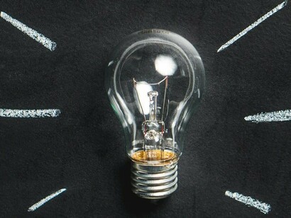 A light bulb placed in the center of a chalkboard with lines radiating outwards creates a visual representation of an idea or inspiration and how it can illuminate the way forward