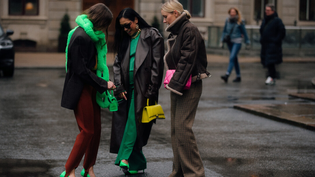 Estilista encontra as amigas enquanto usa um cachecol verde na forma de uma corrente em alusão ao compromisso com a sustentabilidade