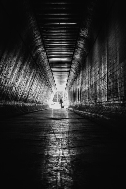 Figure moving through a shadowed tunnel toward a distant light, representing the journey from uncertainty to meaning