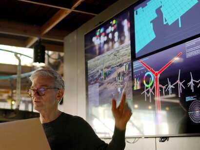 An expert attends a renewable energy seminar with information displayed on a large screen
