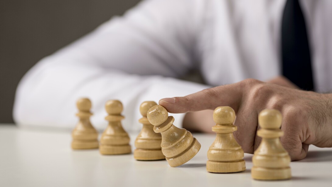 Un uomo d'affari spinge un pedone degli scacchi, creando un effetto domino che fa cadere gli altri, simboleggiando decisioni strategiche o l'impatto di una singola azione