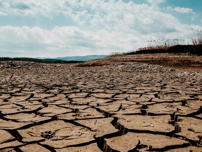 Cracked earth beneath a partly cloudy sky, emphasizing dryness and environmental strain