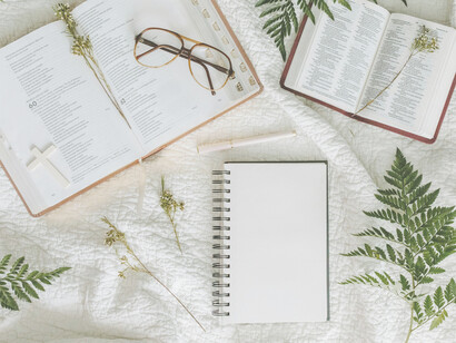 Un par de libros y elementos religiosos, una libreta, una lapicera, unos anteojos y unas ramitas de helecho sobre una tela blanca