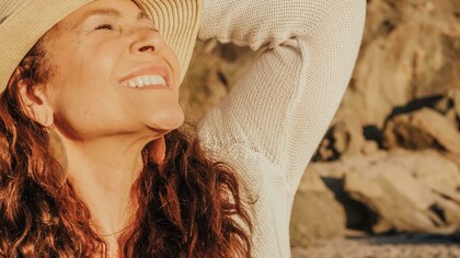 A smiling woman with a hat relishes in the sunlught