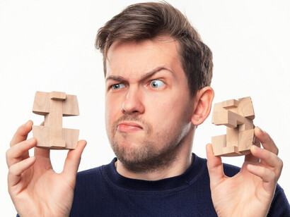 A man, looking confused at a wooden puzzle, reflects the challenges of decision-making, where cognitive biases and emotional influences can complicate the process