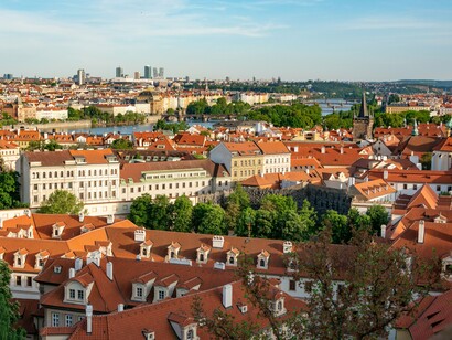 Prague’s old-world rooftops filling the foreground as viewed from above, symbolizing a city where extraordinary stories can remain hidden in plain sight