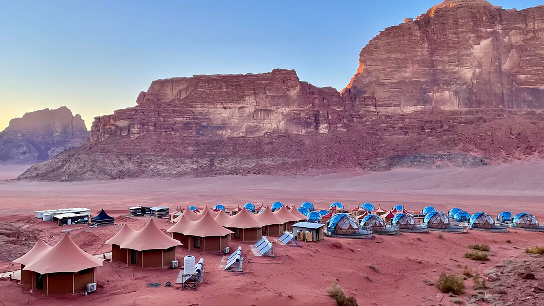 A desert landscape with traditional Bedouin tents and surrounding mountains can be seen in Wadi Rum, Jordan