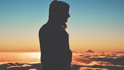Silueta de una mujer con capucha frente a un idílico atardecer