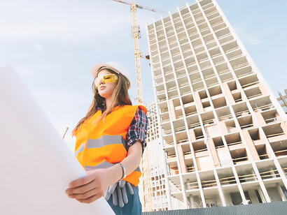 Woman carefully examining construction draft on the site, consulting the blueprint, emphasizing attention to detail and dedication