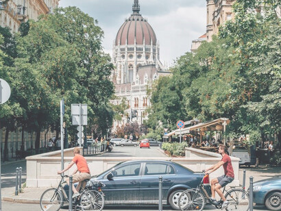 Pedestrians stroll along the bustling sidewalks of Budapest, Hungary, amidst the city's vibrant daytime energy, flanked by cars and architectural marvels
