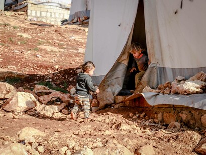 Two Syrian refugee children go into their tent in a refugee camp