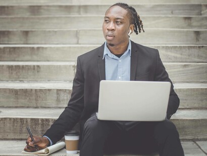 A man on the steps of a building in Africa using the internet while thinking about its connectivity issues