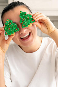 A woman decorates gingerbread cookies shaped like Christmas trees in the kitchen