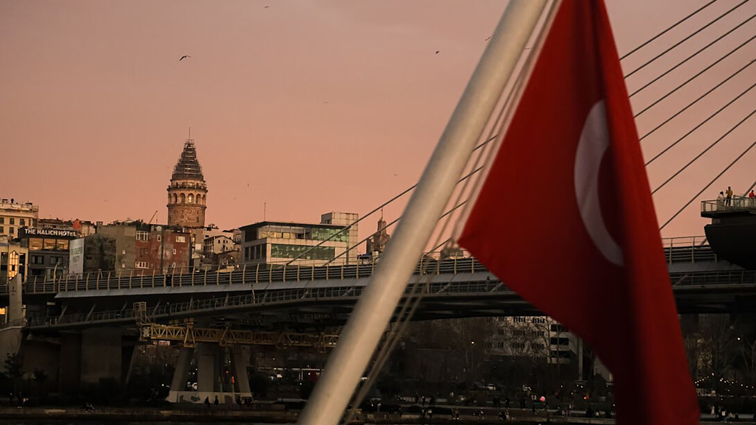 A red and white Turkish flag waves proudly above a bridge and buildings, symbolizing the heart of Türkiye