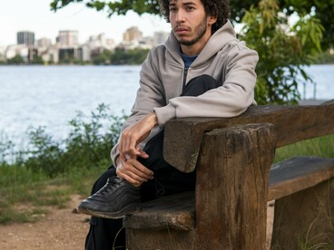 A young man retreating into himself while sitting alone outdoors, reflecting the tendency to push inward and shut others out before they can leave