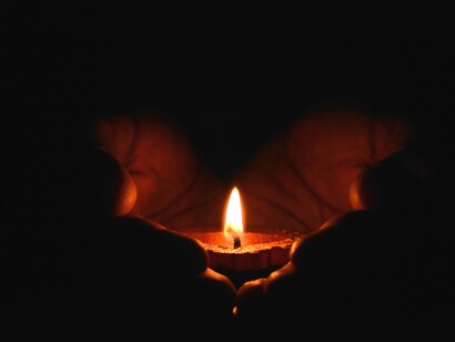 Mãos seguram uma vela em direção a um oratório