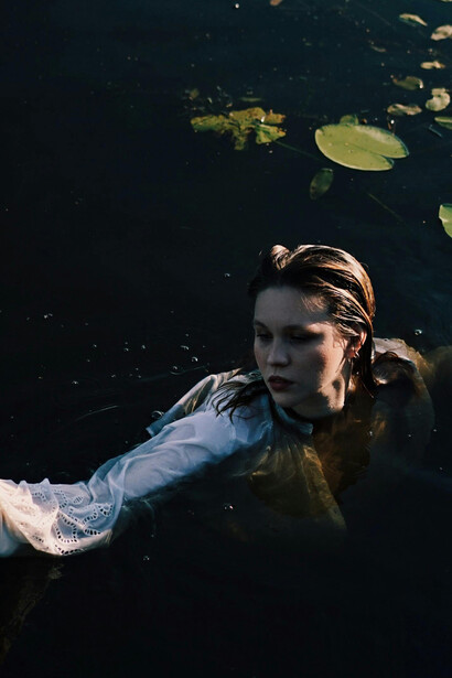 A serene woman floating on still water, embraced by delicate lotus flowers
