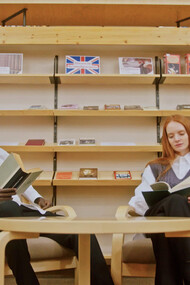 In a quiet corner of the library, two readers immerse themselves in the transformative power of knowledge, proving that true growth begins with intentional investment in oneself