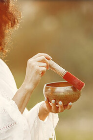 A woman holding a chanting bowl in a natural setting, embodying Ayurveda and a healthy lifestyle