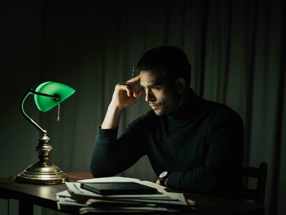 An elegant man reading a book at a table illuminated by a retro lamp