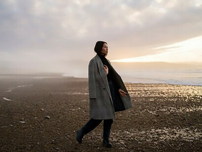 Alone on the shore, a woman drifts through waves of nostalgia