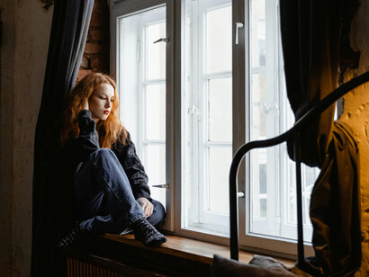 A stressed woman sitting on a window sill, lost in thought