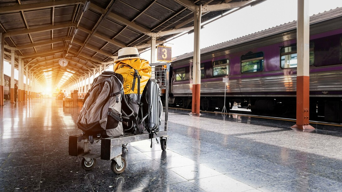Bagagens aguardam ao lado de um trem em uma estação iluminada pelos primeiros raios de sol. A imagem representa o momento concreto da partida, enquanto a ansiedade pré-viagem muitas vezes começa muito antes, ainda no espaço íntimo de casa
