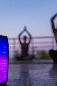 A colorful backlit wireless speaker in the foreground, as a group of friends practices yoga in the background