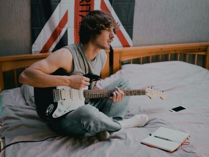 A young man closing his eyes as he strums his guitar and lets the creativity loose