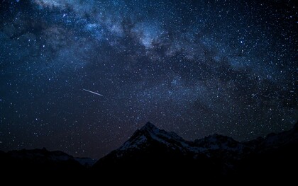 A meteor streaking across the Milky Way above mountains, representing the excitement of peak meteor shower season