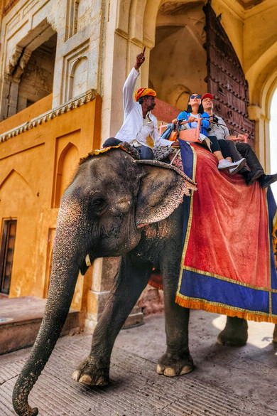 Couple riding an elephant past a vibrant building in Jaipur, Rajasthan, India
