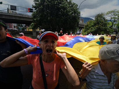A group of people protest while holding a giant Venezuelan flag