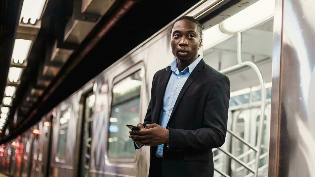 Confident young man in a suit using a smartphone while standing on a subway platform in a modern urban setting