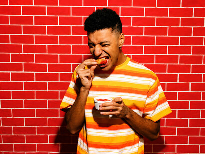 A young man savours crispy hot chicken while embracing the fiery spice and intense flavour of the meal