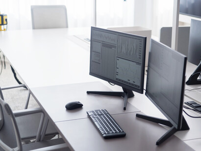 Escritório moderno equipado com computadores cujos monitores exibem gráficos e indicadores de desempenho. A visualização de dados facilita a análise de custos e a identificação de oportunidades de optimização
