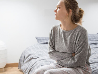 A woman suffering from food intolerances sitting in bed, pressing her hands on her stomach as she endures painful symptoms from food allergies