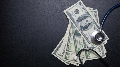 A stethoscope lying on currency bills, representing how the healthcare industry is often driven by profit and financial incentives rather than patient care