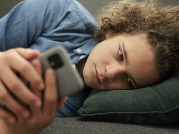 Adolescente utiliza o celular sozinho no sofá enquanto navega pelas redes sociais. A exposição contínua a estímulos extremos pode impactar empatia, impulsividade e percepção de risco. O ambiente doméstico nem sempre revela o que acontece nas telas. Muitos conteúdos violentos circulam silenciosamente nos espaços digitais frequentados por jovens