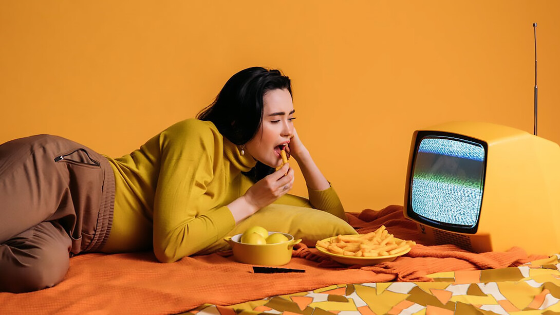 Woman lying on orange floor looking at television