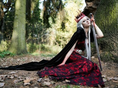 A woman standing near a tree, dressed in fantasy-style clothing