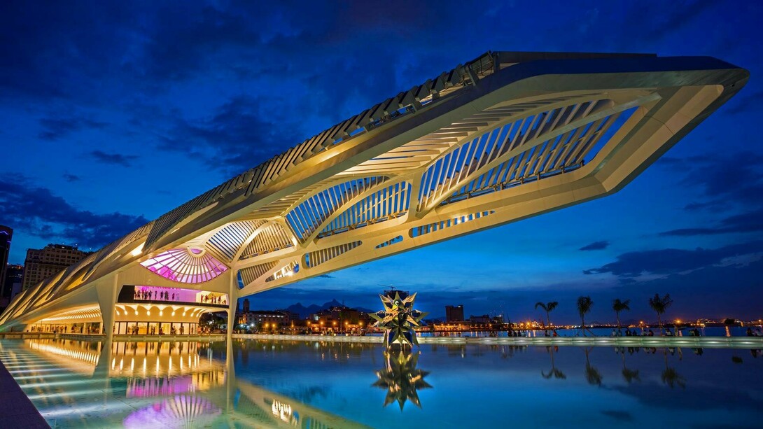 O Museu do Amanhã se projeta sobre o espelho d’água da Praça Mauá, iluminado contra o céu azul do início da noite. A arquitetura de Santiago Calatrava transforma o edifício em um dos símbolos mais marcantes do Rio de Janeiro contemporâneo