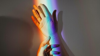 Two hands hold each other with a rainbow passing through