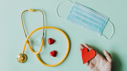 A stethoscope, a face mask and a hand holding a heart