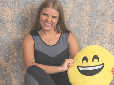 A young, sporty girl in athletic attire, holding a smiling emoji pillow