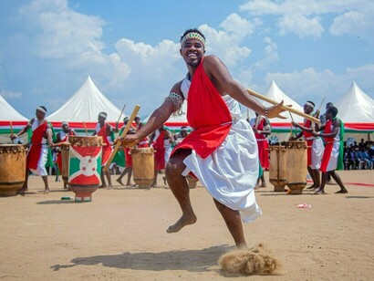 Un artiste burundais dansant en costume traditionnel devant des tambours de cérémonie, symbolisant la force des traditions culturelles